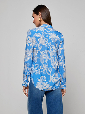 A woman with straight brown hair, facing away from the camera against a plain light background, wears the Holly Blouse in regatta blue and white paisley print with long sleeves and button down front, paired with blue jeans.