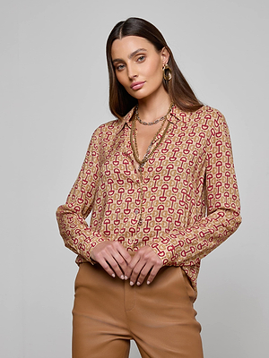 A woman with long brown hair wears the L'AGENCE Holly Blouse featuring a slim fit and horse bit print, styled with tan pants and layered gold jewelry. She stands against a plain light gray background with a neutral expression.