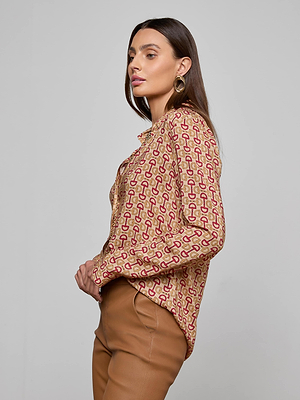 A woman with long brown hair wears the L'AGENCE Holly Blouse, a slim fit, long sleeve button down with a horse bit print, along with brown pants and gold hoop earrings, shown in profile against a light gray background.