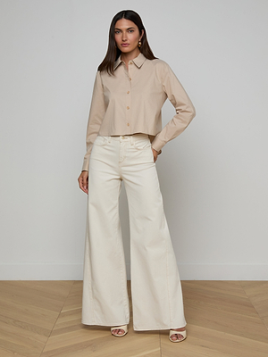 A woman stands indoors against a plain wall in the Cosette Shirt and high-waisted, wide-leg cream pants with open-toe heels. Her long, straight hair and neutral expression highlight the refined structure of the shirt.