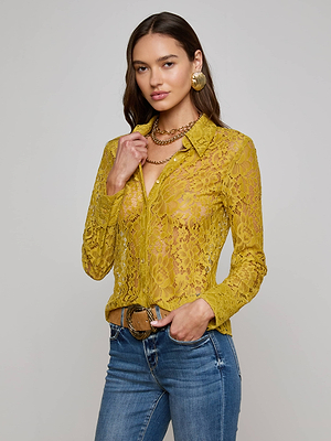 A woman with long brown hair confidently poses against a light background wearing the Maia Floral Lace Blouse by L'AGENCE, styled with blue jeans, gold hoop earrings, and a chain necklace.