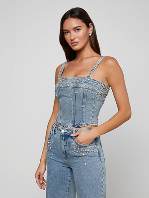 Woman wearing a denim top and pants with embellishments on a gray background