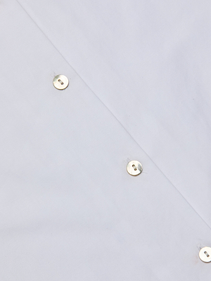 Close-up of the Deon Tie-Neck Blouse crafted from white organic cotton poplin with metallic snap buttons, featuring a smooth, slightly glossy finish—perfect for oversized tie-neck designs and blouson sleeve styles.