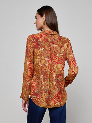A woman with long brown hair and gold hoop earrings is seen from behind wearing the L'AGENCE Nina Silk Blouse—a relaxed fit button down with a golden paisley pattern—and dark blue jeans against a light, plain background.