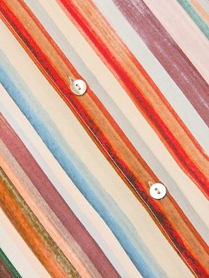 Close-up of the Nina Silk Blouse's relaxed fit fabric, displaying diagonal multicolored stripes in red, blue, orange, and beige tones, with two white buttons sewn along a stripe.