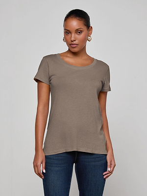A woman with dark hair pulled back wears gold hoop earrings and the L'AGENCE Cory Cotton Scoopneck Tee in taupe with a relaxed fit, paired with dark blue jeans, standing against a plain light gray background and looking at the camera.