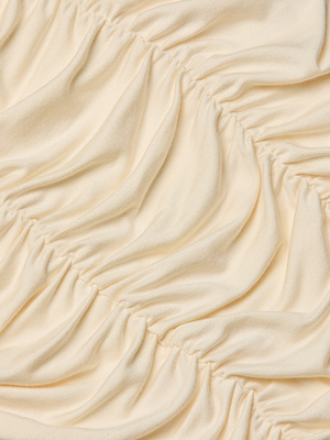 Close-up of the Baliegh Ruched Bodysuit in vintage white, highlighting gathered stitching that forms wavy, textured folds and curved lines on the fabric.