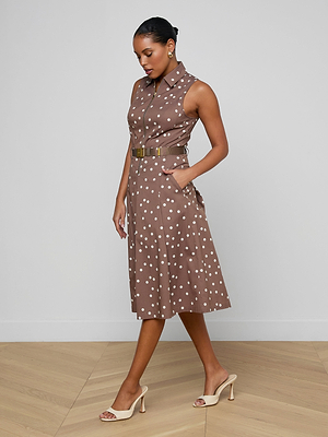 Woman wearing a brown polka dot dress on a light wooden floor with a white wall background