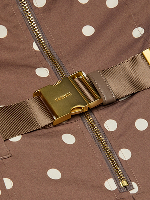 Close-up of a gold zipper and buckle on a brown fabric with white polka dots