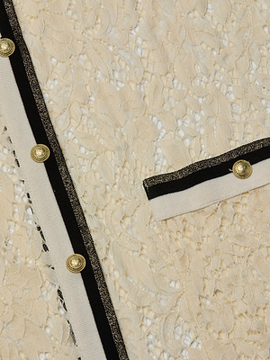 Close-up of the Whisper Lace Cardigan Dress, featuring cream lace fabric, chic scalloped edges, black and white trim, gold buttons, and a matching pocket with coordinating trim and button detail.