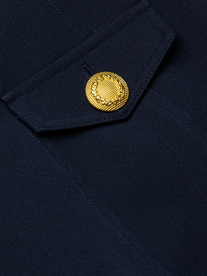 Close-up of the Cori Mini Dress in navy blue, featuring a flap with gold-tone emblem hardware and textured edge. The button on the flap adds structure, giving the dress a formal look.