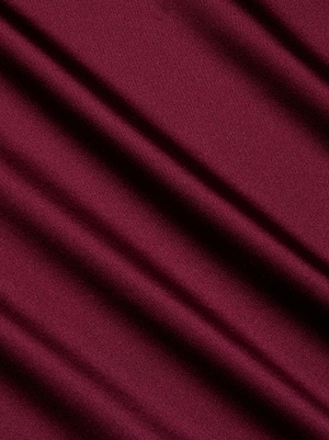 The Sayla Silk Gown by L'AGENCE features rich maroon fabric in soft, diagonal folds, casting gentle shadows and highlighting its smooth, elegant texture for a touch of vintage glamour.