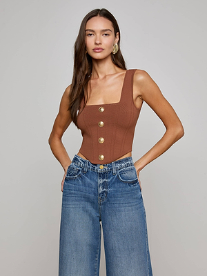 A woman wears the chocolate brown Saga Top with gold buttons and high-waisted blue wide-leg jeans, standing with her hands in her pockets against a plain light gray background.