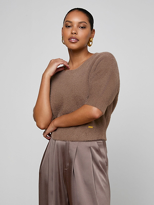 A woman poses against a plain background, wearing the Guinevere Cropped Pullover in brown and taupe satin pants. Her hair is pulled back, she accessorizes with gold hoop earrings, and poses with one hand near her neck, the other by her waist.