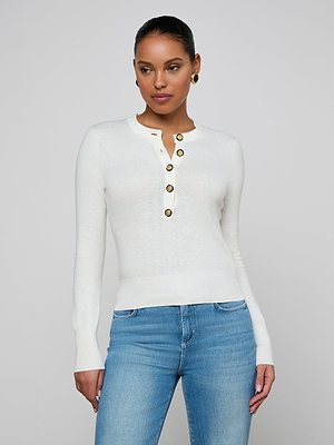 A woman in the white Ronda Knit Henley Top with gold button placket and light blue jeans stands against a plain light gray background, looking slightly to her left.