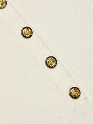 Close-up of the Ronda Knit Henley Top’s lightweight white fabric, highlighting a diagonal row of four gold decorative buttons with intricate raised designs and black-accented rims.