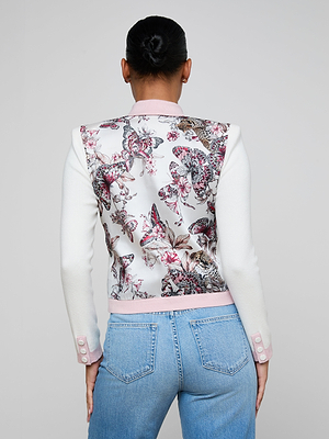A woman with her hair in a bun is seen from the back, wearing a white and pink Nomi Satin Back Cardigan with butterfly-jungle print and contrast trim, paired with light blue jeans.