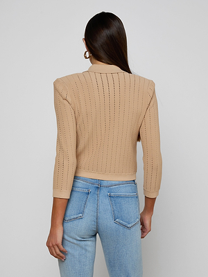 A woman with long brown hair and gold hoop earrings wears the Risa Collared Cardigan in neutral tan and light blue jeans, standing with her back to the camera against a plain light background.