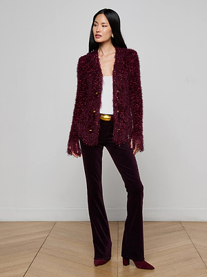 A woman with long straight black hair stands indoors against a plain background, wearing a white top, a textured burgundy jacket, and the Stevie Velvet Jean—classic fit, straight leg stretch velvet pants—with matching heeled boots.