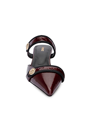 Front view of the L'AGENCE Gilliane Heeled Mule, showcasing a vintage-contemporary design with glossy wine patent leather, two black and gold-accented straps, and bold lion-embossed buttons.