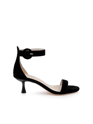 The Andelle Kitten-Heel Sandal is a black suede shoe with a low, curved heel, open toe, single toe strap, and an ankle strap topped with a large round buckle, shown against a white background.