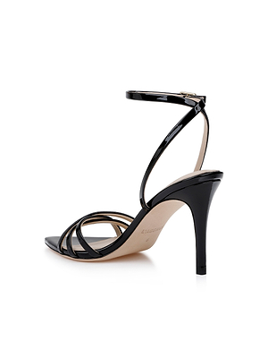 The Dua Leather Sandal, shown from a rear-side angle against a white background, is crafted in black patent leather with an open toe, thin ankle strap, and three slim front straps in a strappy design.