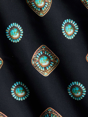 A close-up of the Vanessa High-Waisted Bikini Bottom shows its geometric medallion print in turquoise and brown on black, featuring circular and diamond shapes for a vintage, decorative look.