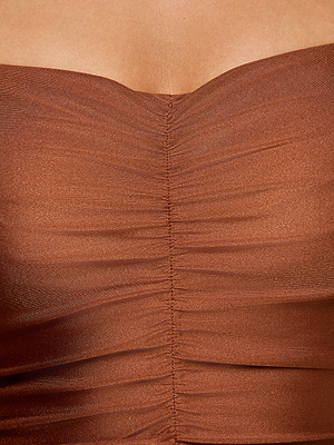 A close-up of a person wearing the Aubrey Ruched One-Piece Swimsuit in bronze shimmer, highlighting the textured shirring and gathered fabric detail at the center of the upper chest.