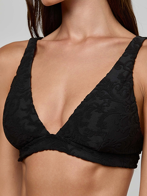 A woman is wearing the Lexie Bikini Top, a black jacquard terry bralette featuring a deep V-neckline and wide straps. Only her upper torso and part of her face are visible.