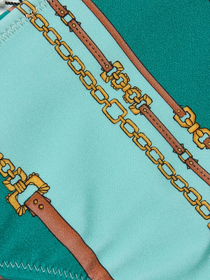 A close-up of the Jean Bikini Bottom’s four-way stretch nylon shows a gold chain and brown leather strap print on teal and light blue, with visible edge stitching—ideal for a high-leg or sage bikini bottom look.