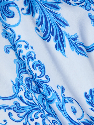 A close-up of the Elise Cover-Up Dress in white fabric with blue baroque floral and leaf patterns, featuring a slightly wrinkled texture—perfect for a water-safe crepe halter midi dress.
