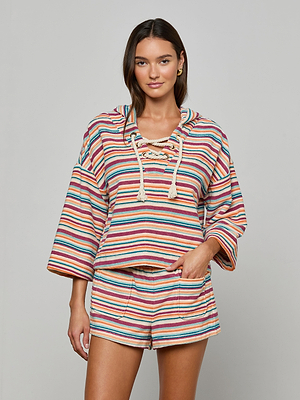 A woman poses against a plain background wearing the Lee Cover-Up Poncho set with colorful stripes, perfect for poolside lounging. She has her right hand in her pocket and is smiling slightly.