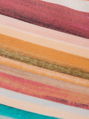 A close-up of the Britt Tie-Side Bikini Bottom shows its soft fabric with horizontal stripes in red, orange, green, teal, and beige, featuring adjustable tie sides for a colorful and textured look.
