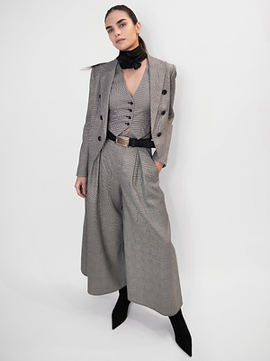 A person stands against a white background in a grey suit with a long blazer, wide-leg trousers, belted vest featuring the Cebo Belt, black neck scarf, and black boots—a look ready for New York Fashion Week Fall 2026.