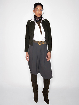 A woman poses against a white background in a black jacket, white shirt, gray pleated culottes, the Yarros Belt, patterned scarf, and knee-high black boots—a look inspired by Fall 2026 New York Fashion Week trends.