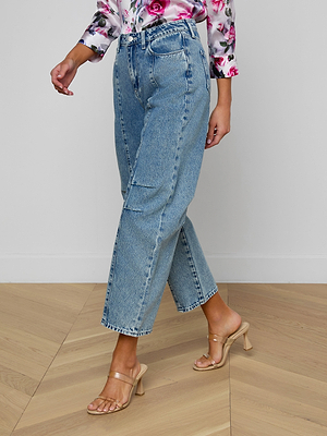 A person wearing Reba Rodeo Jeans, a floral long-sleeve blouse, and beige heeled sandals walks on a wooden floor. The image is cropped to display the lower torso and legs.