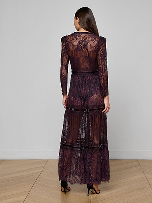 A woman stands indoors, back turned, wearing the Poe Lace Maxi Dress in dark purple with velvet trim and tiered lace layers, paired with black high-heeled sandals for a vintage-inspired look.