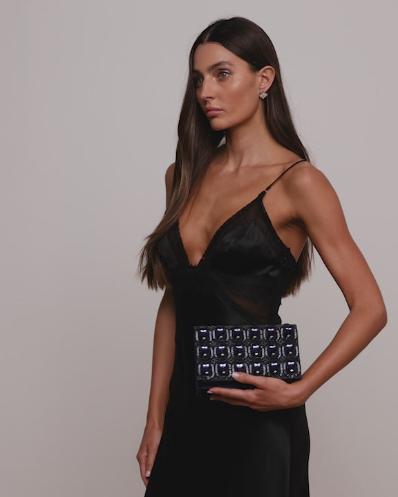 Blue and black sparkly embellished clutch bag with emerald looking stones being held by model wearing a black dress