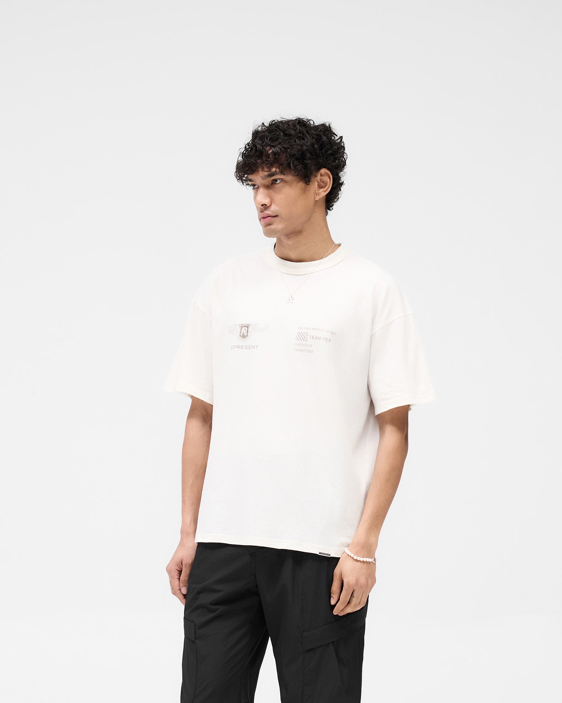 Man wearing a white t-shirt on a plain white background | Team Rep T-Shirt in Flat White | Oversized t-shirt with Represent logo metal bar | SS25 T-Shirts | Represent Clo