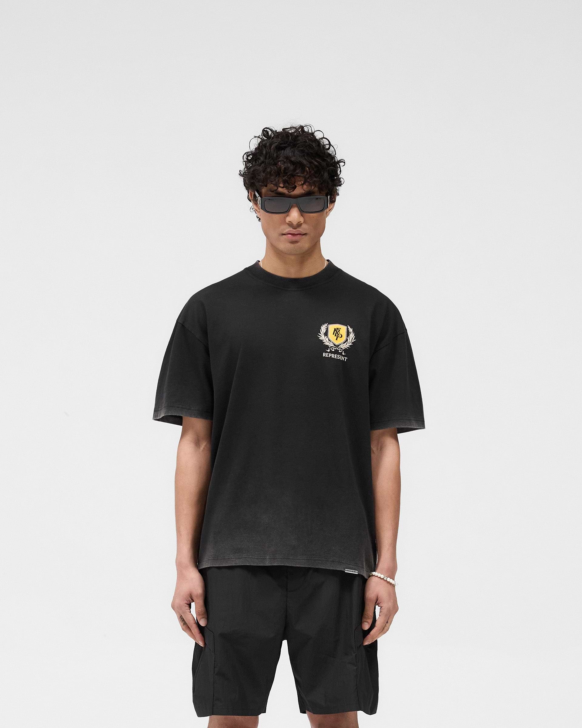 Man wearing a black graphic t-shirt on a plain white background | Crest T-Shirt in Vintage Black | Oversized tee with crest graphic and fade-out wash | SS25 T-Shirts | Represent Clo