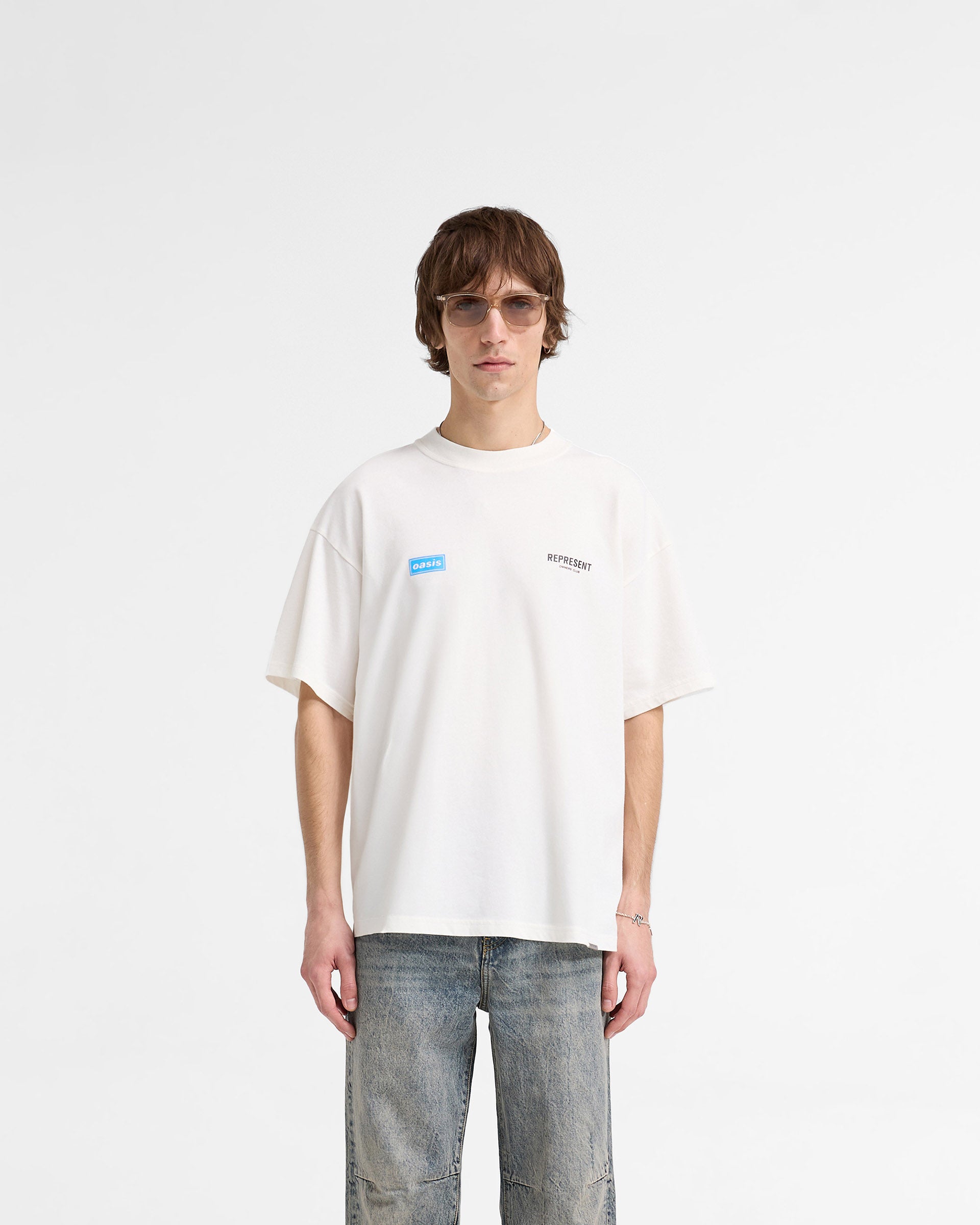 Man wearing a white t-shirt on a plain white background | Represent X Oasis Owners Club T-Shirt in Flat White | Oversized t-shirt with Oasis artwork | FW24 T-Shirts | Represent Clo