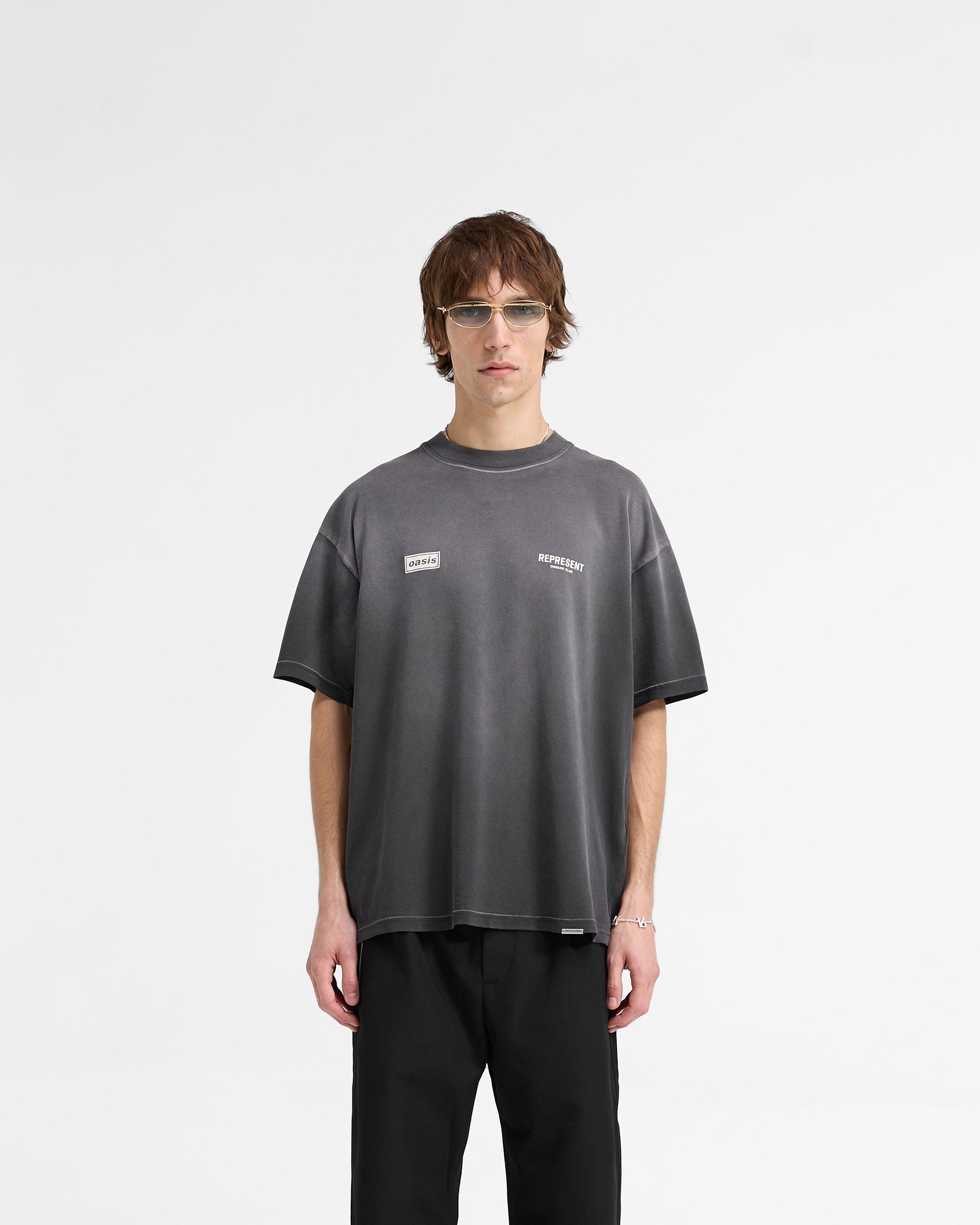 Man wearing an oversized black t-shirt on a plain white background | Represent X Oasis Owners Club T-Shirt in Stained Black | T-shirt with fly postered Oasis artwork and dual front logos | FW24 T-Shirts | Represent Clo