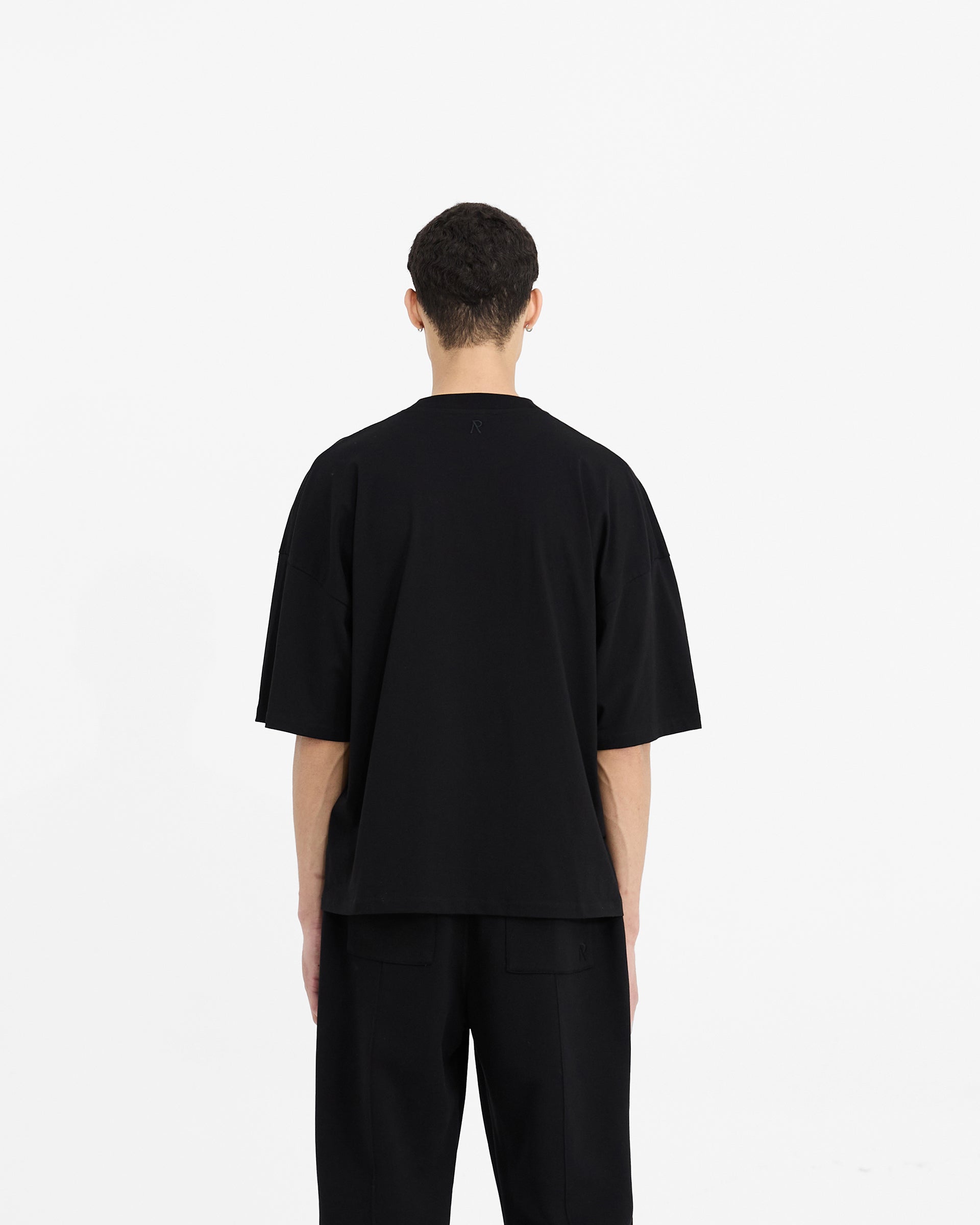 Man wearing an oversized black t-shirt on a plain white background | Initial Boxy T-Shirt in Black | Super oversized and boxy cropped t-shirt | Initial T-Shirts | Represent Clo