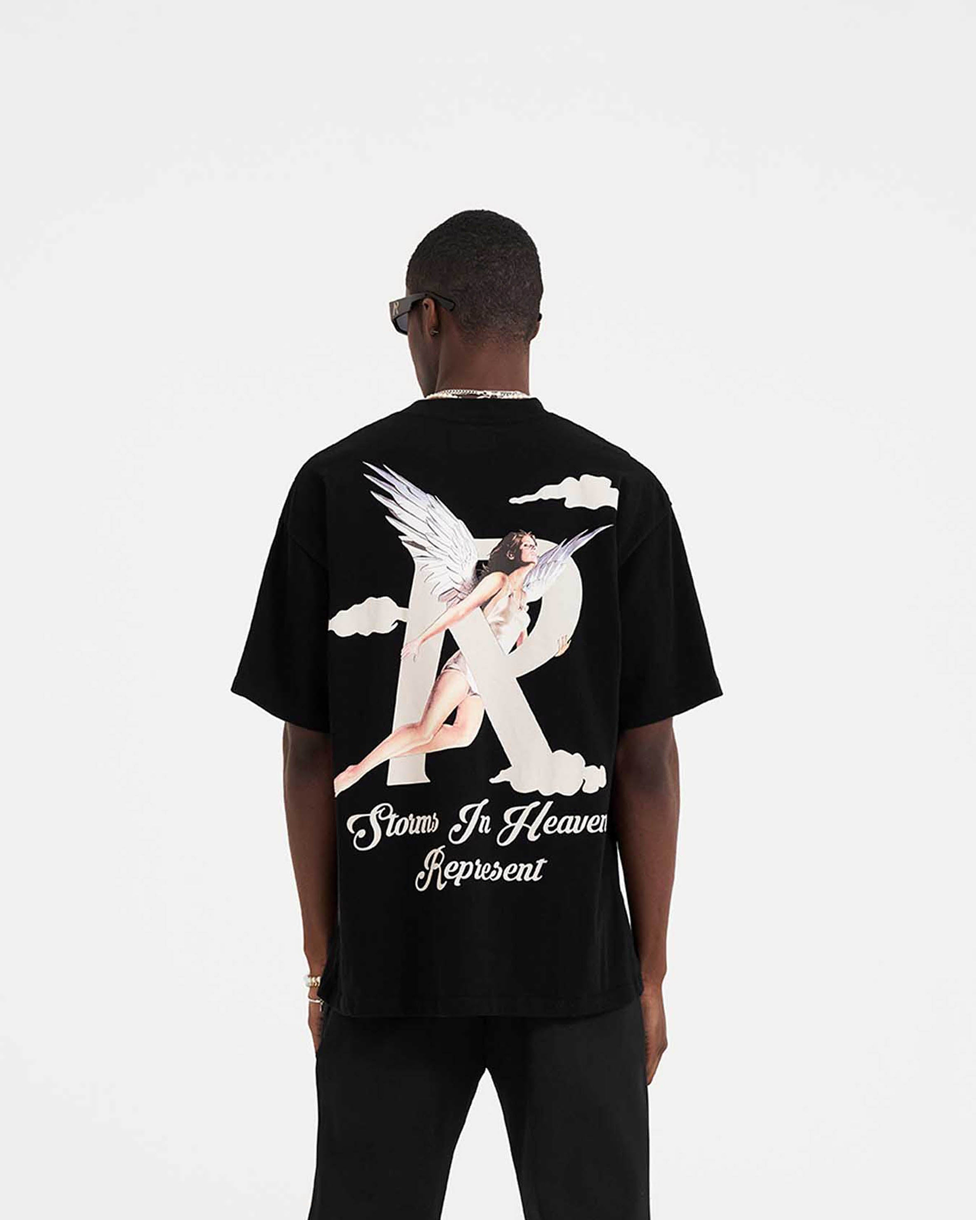 Man wearing a black t-shirt with chest and back graphics on a plain white background | Storms In Heaven T-Shirt in Black | Oversized fit short sleeve t-shirt | SS23 T-Shirts | Represent Clo