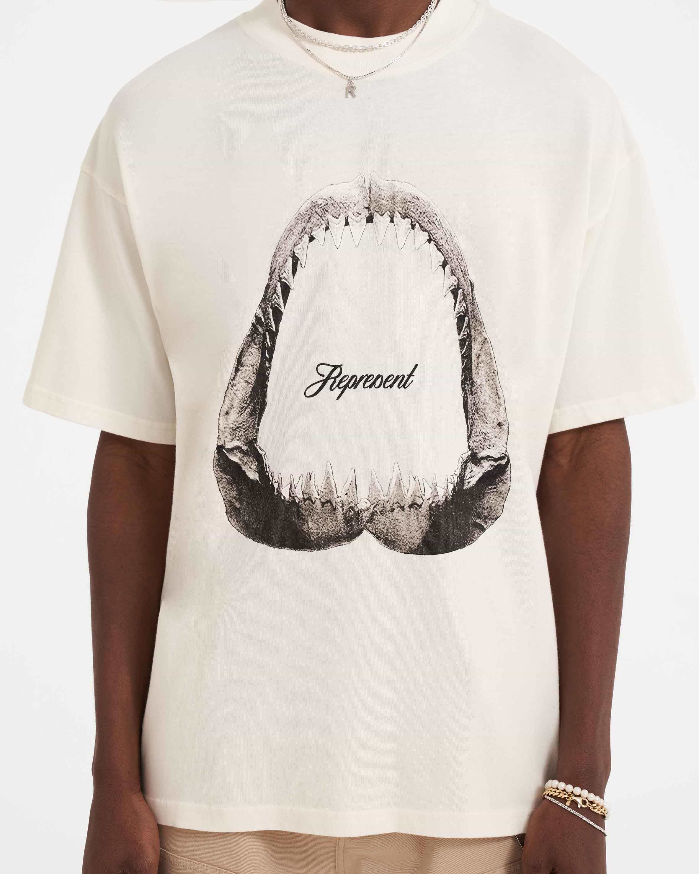Man wearing a white graphic t-shirt on a plain white background | Shark Jaws T-Shirt in Flat White | Oversized graphic t-shirt with ribbed crewneck | SS23 T-Shirts | Represent Clo