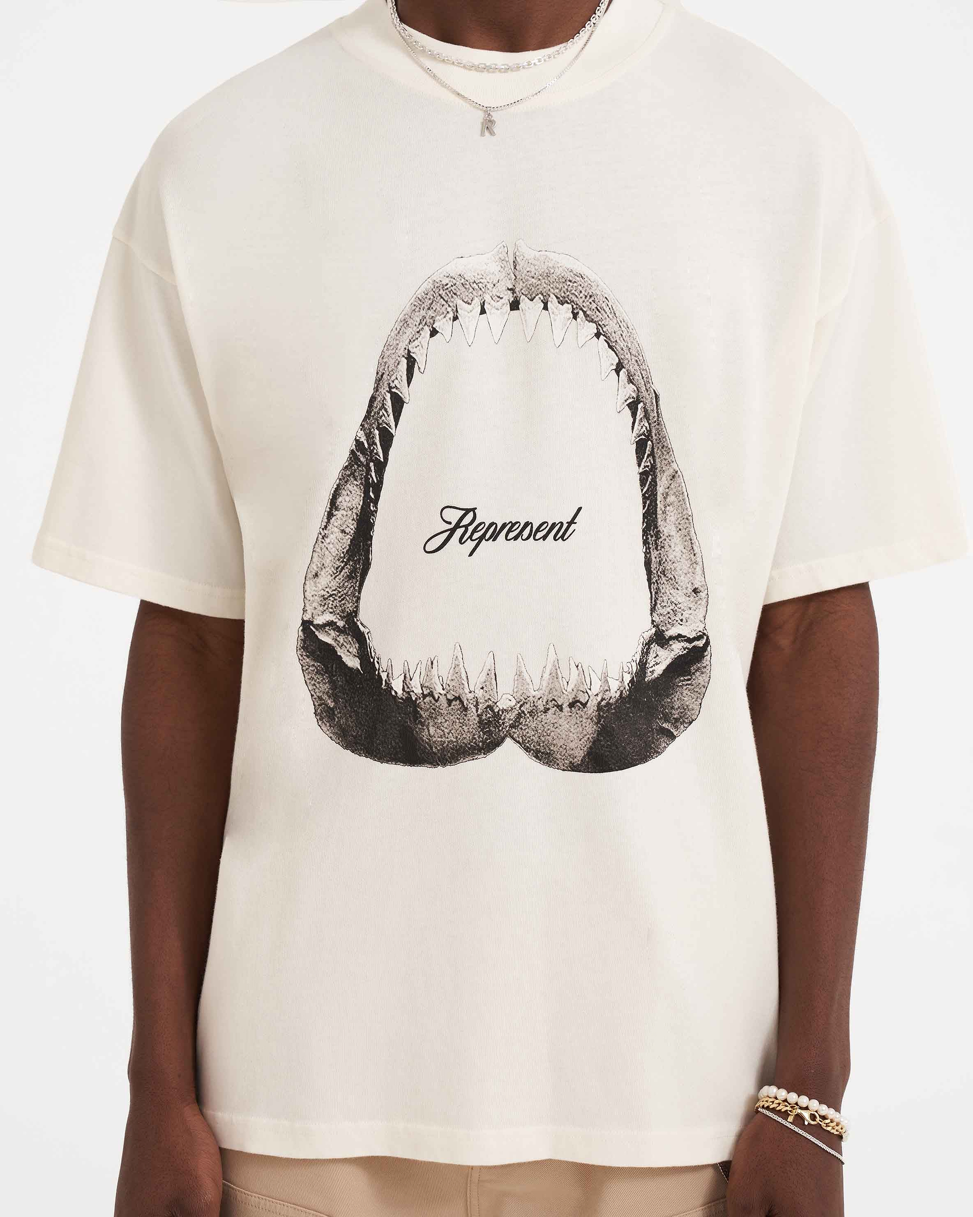 Man wearing a white graphic t-shirt on a plain white background | Shark Jaws T-Shirt in Flat White | Oversized graphic t-shirt with ribbed crewneck | SS23 T-Shirts | Represent Clo