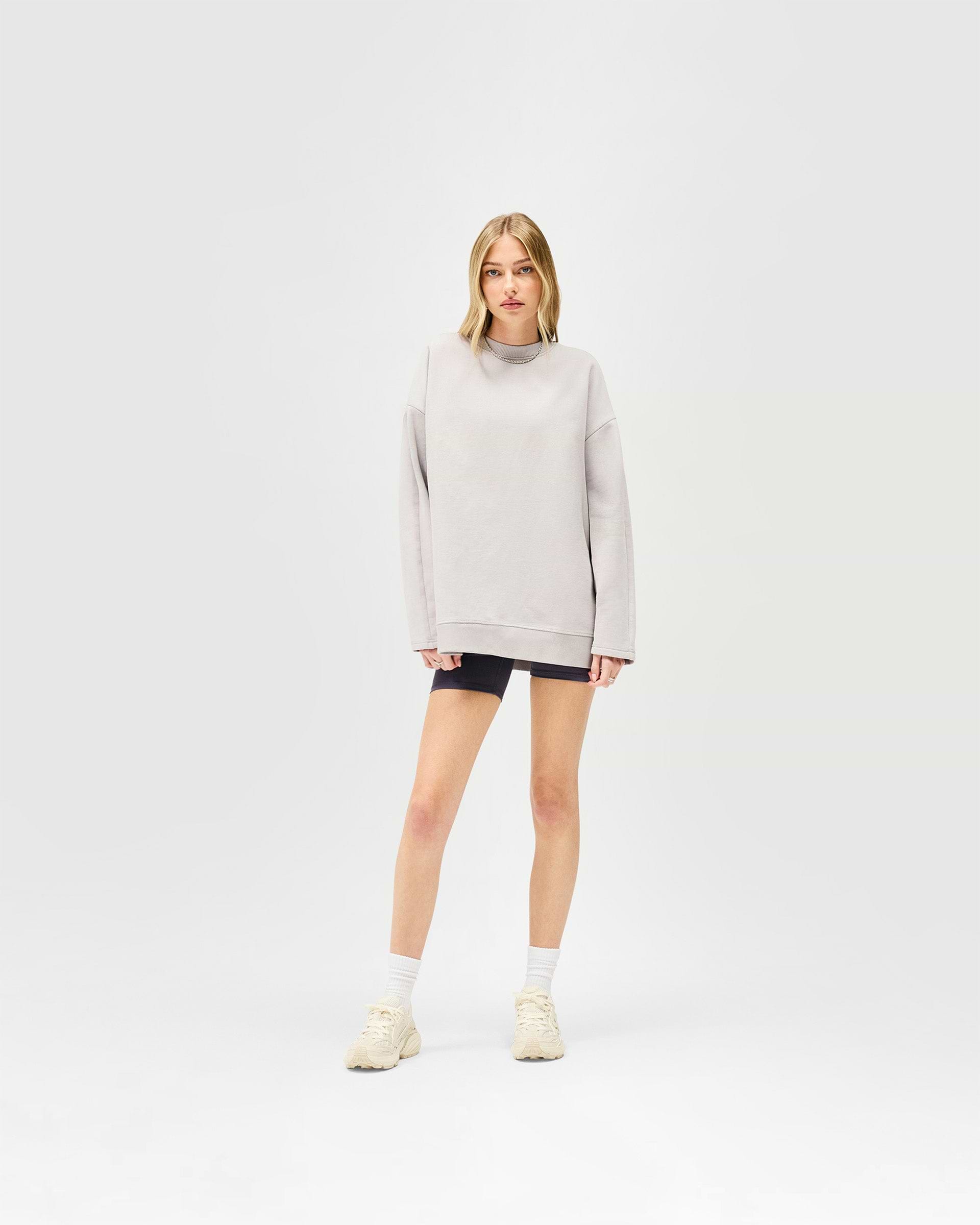 Woman wearing a light grey oversized sweater on a plain white background | Epic Raglan Sweater in Light Grey | Oversized fit raglan sleeve sweater with raw edge applique branding | Womens SS25 Sweaters | Represent Clo