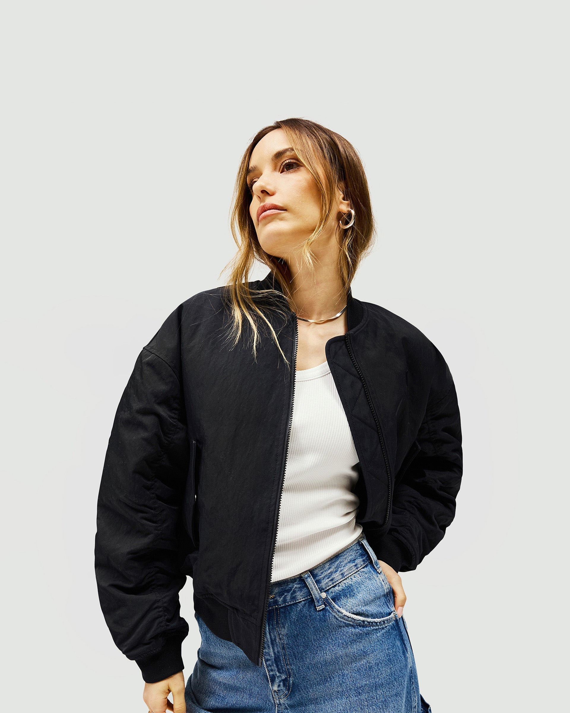 Woman wearing an oversized black bomber jacket on a plain white background | Subway Jacket in Jet Black | Nylon bomber with ribbed cuffs and embroidered logo | Womens SS25 Outerwear | Represent Clo
