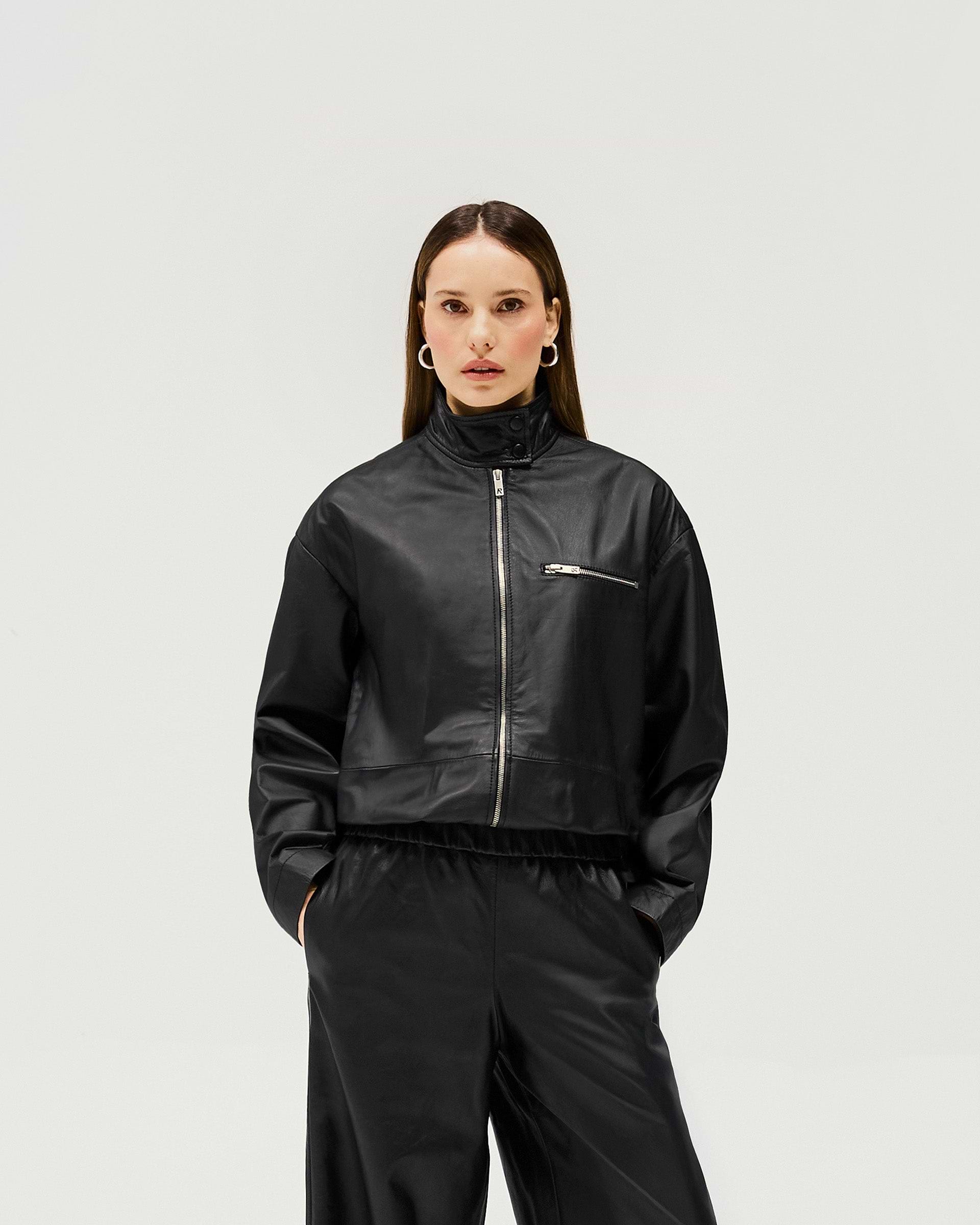 Woman wearing a black leather jacket on a plain white background | Fuel Jacket in Jet Black | Leather jacket with 2 way zip and elasticated hem | Womens SS25 Outerwear | Represent Clo