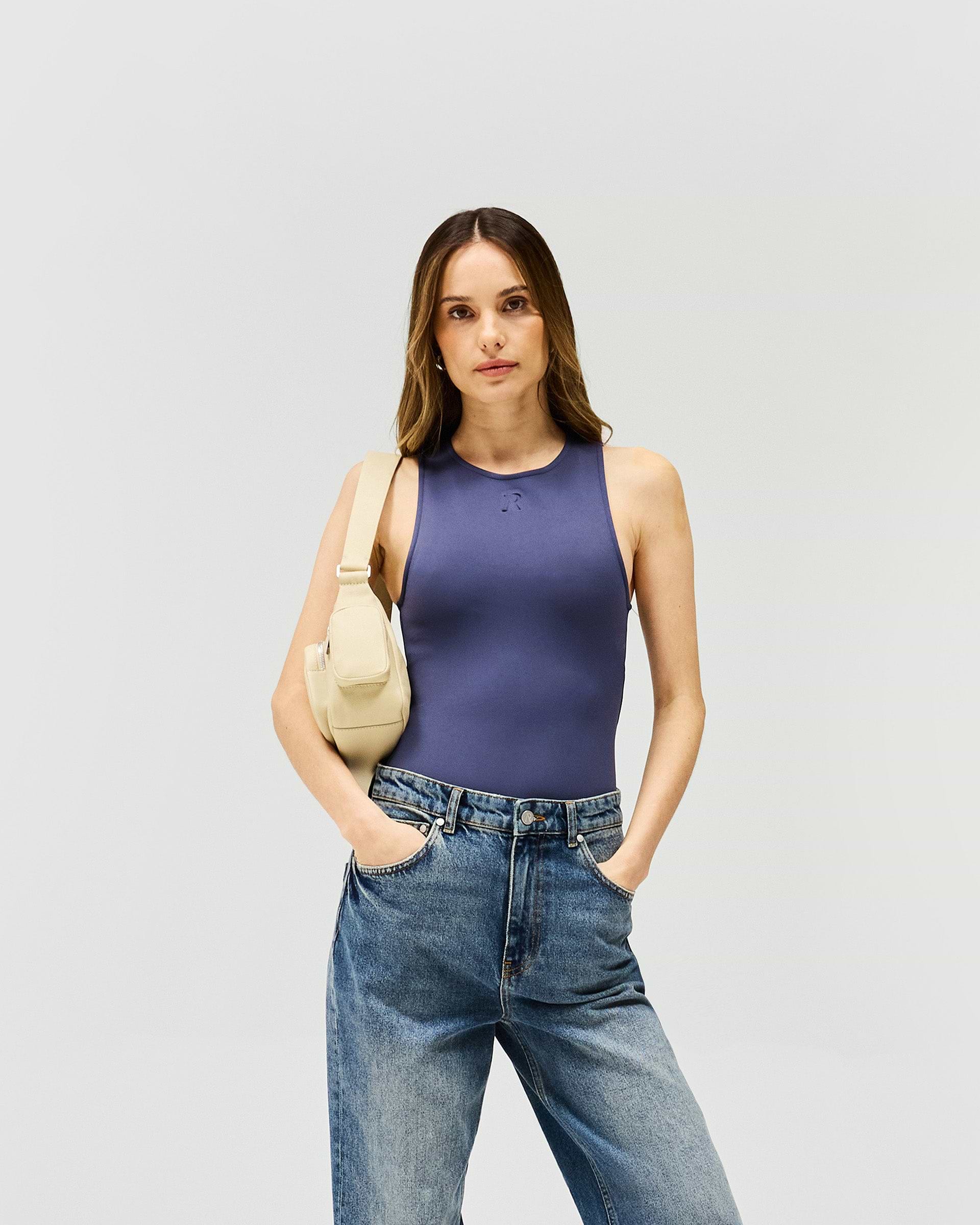 Woman wearing a grey minimalist bodysuit on a plain white background | Control Bodysuit in Graphite | Bodysuit with rounded neckline and thong back | Womens SS25 Tops | Represent Clo